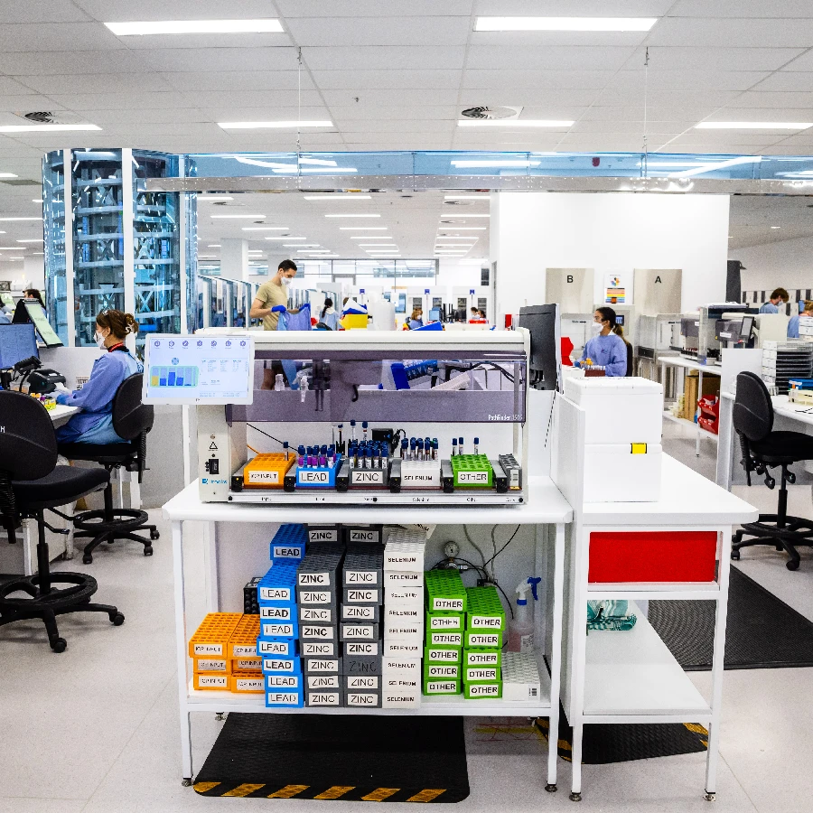 A modern laboratory with staff working at desks and stations; boxes labeled with various elements are organized on a central cart, highlighting the efficiency brought by lab automation.